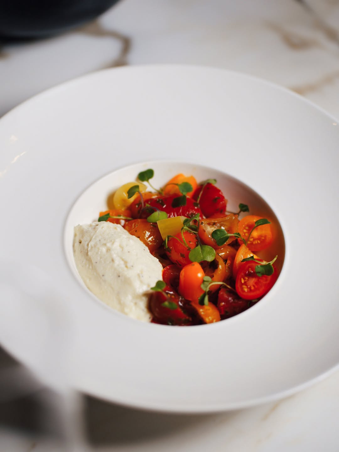 Plato de tomates de varios colores acompañado de una preparación cremosa