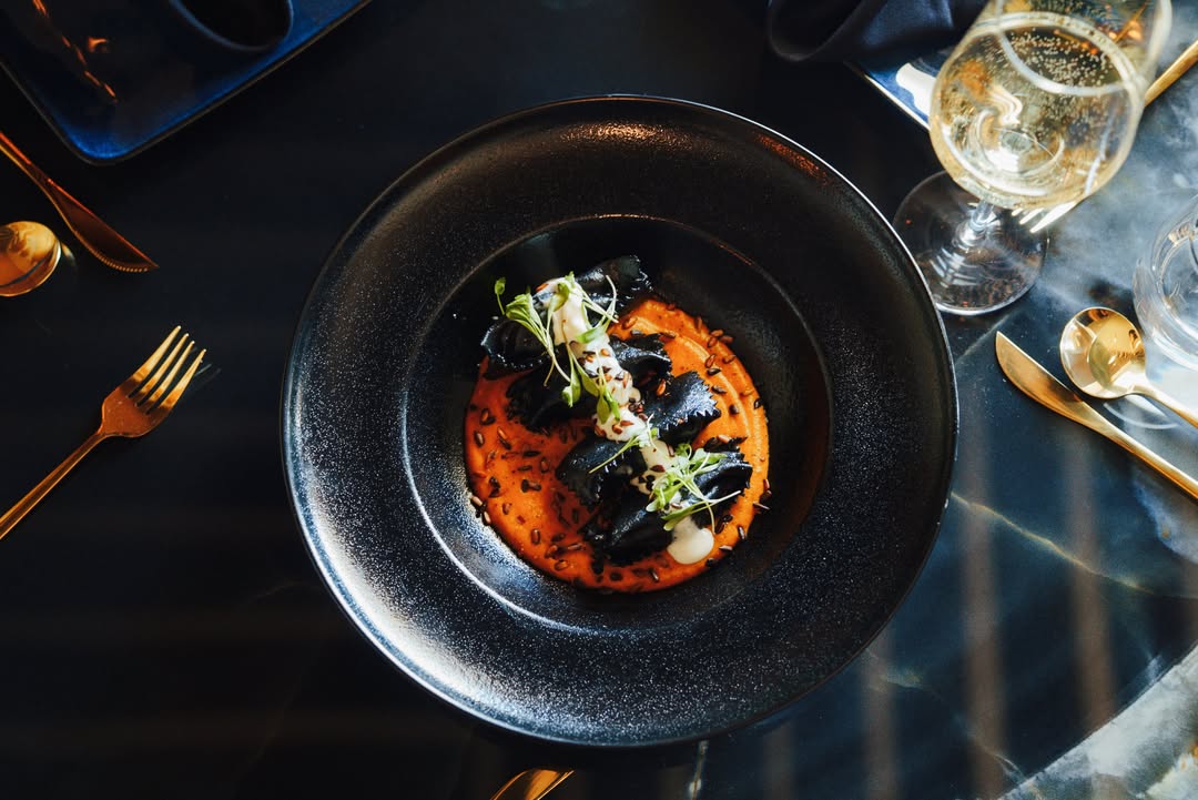 Plato negro con una preparación oscura sobre salsa naranja en una mesa servida