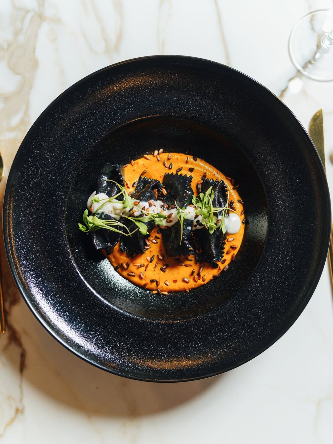 Preparación oscura presentada sobre salsa naranja en un plato negro